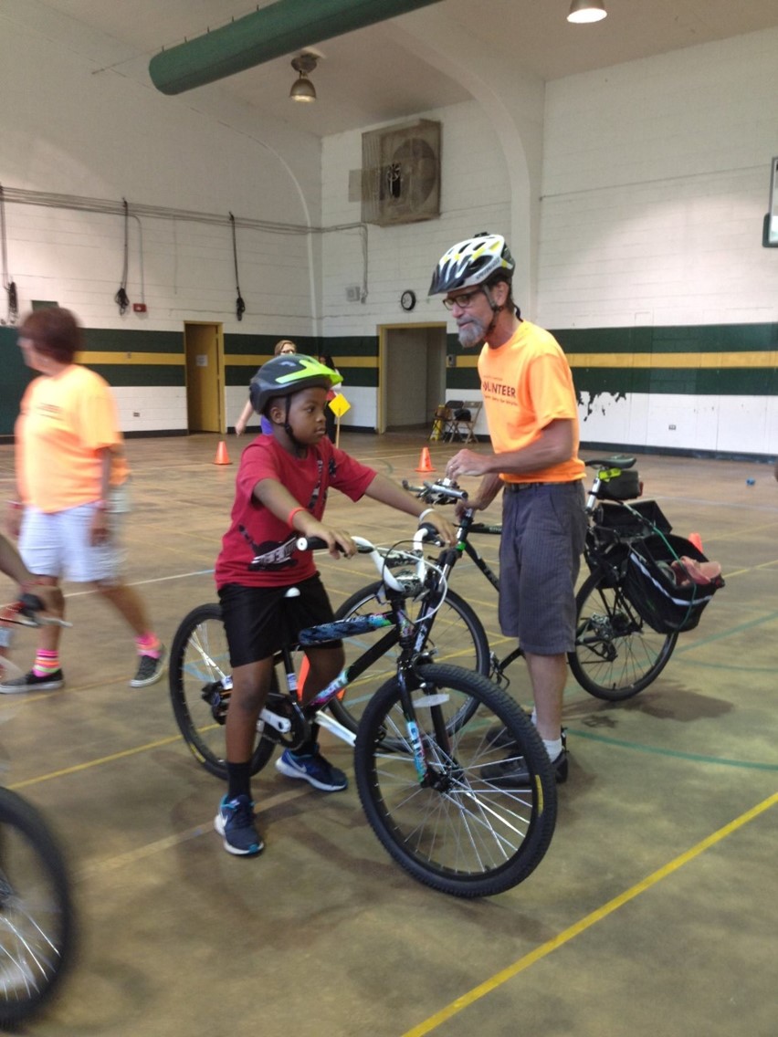 Volunteers teaching children about safe ways to bike to school. Child in foreground on a bicycle.