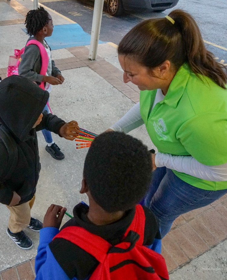Volunteer handing out pencils to children.